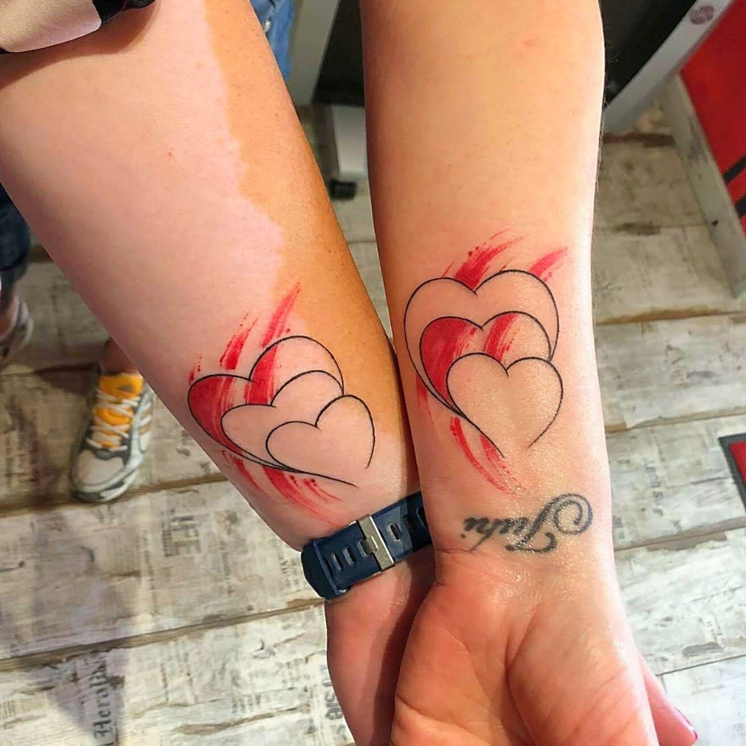 Matching tattoos with three overlapping hearts and a red brushstroke background, symbolizing love, unity, and closeness